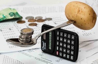 Budget personnel. Une calculatrice sur la tranche avec une cuillère en équilibre dessus supportant d'un côté une pomme de terre et de l'autre des pièces de monnaie.