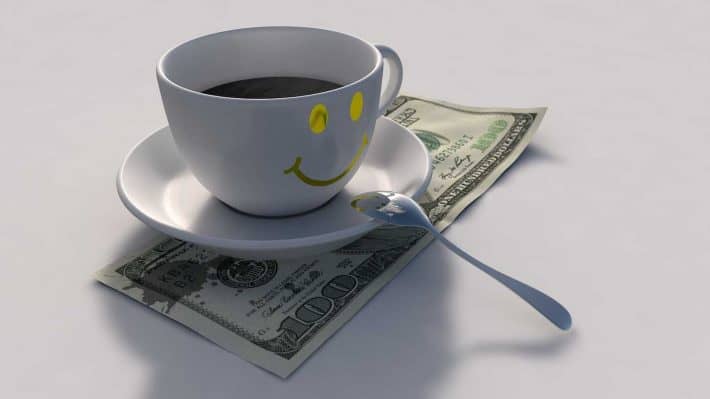 Comment faire des économies de façon intelligente. Une tasse de café souriante sur un billet de 100 dollars.