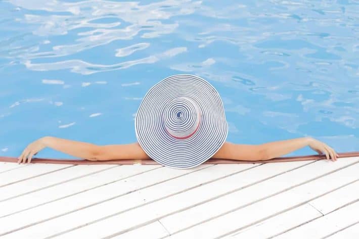 combien d’argent faut-il pour vivre sans travailler. Une femme sur le bord d'une piscine avec un chapeau de pailles.